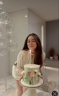 a woman is holding a cake with a candle in it and blowing out the candles