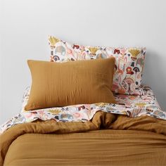 a bed with an orange comforter and two pillows on top of it in front of a white wall