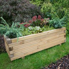 a large wooden planter filled with lots of green plants and flowers on top of grass