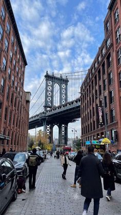 people are walking on the sidewalk in front of some tall buildings with a bridge above them