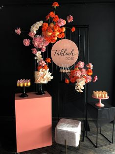 a table topped with cakes and flowers on top of a wooden floor next to a black wall