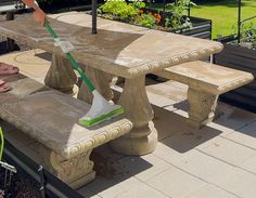 a person with a mop on top of a cement picnic table in the middle of a garden