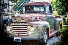 an old, rusty truck parked on the side of a road next to a wooden fence