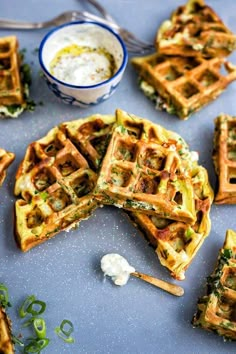 several waffles are arranged on a blue surface with a bowl of ranch dressing in the background