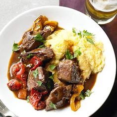 a white plate topped with meat and vegetables covered in gravy next to a glass of beer