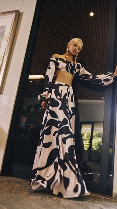 a woman standing in front of a door wearing a black and white dress with long sleeves