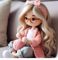 a crocheted doll sitting on a couch holding a ball of yarn and knitting needles