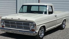 an old white pickup truck parked in front of a garage