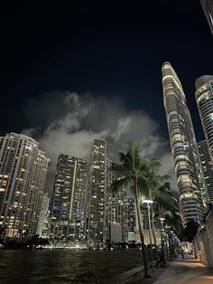 the city skyline is lit up at night with clouds and palm trees in the foreground