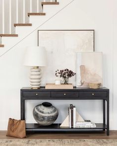 a black table with two vases and a lamp on it next to a stair case