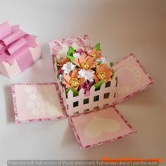 an open box with some flowers inside and a pink bow on the top that is attached to it