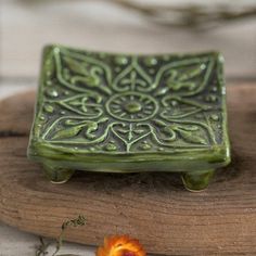 a small green ceramic object sitting on top of a wooden board next to a flower