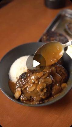 a spoon scooping gravy over rice in a bowl on a wooden table