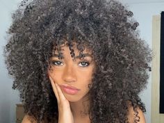 a woman with curly hair is posing for the camera and looking at the camera while holding her hand on her chin