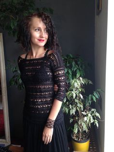 a woman standing in front of a potted plant wearing a black crochet dress