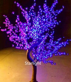 a tree with purple lights on it in the middle of a sidewalk at night time