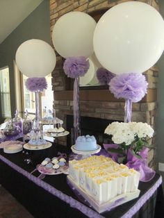 a table topped with cake and balloons next to a fire place filled with cupcakes