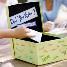 two people sitting at a table with a box that has writing on it and is holding a piece of paper