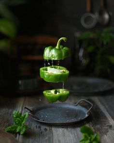 green peppers being dropped from a frying pan on a wooden table with other vegetables