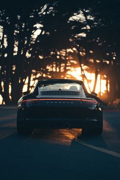 the back end of a black sports car driving down a road with trees in the background