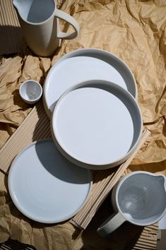 three white plates and two cups on a table with brown wrapping paper behind the plate