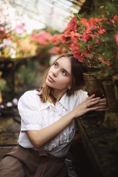 a woman leaning against a wall with flowers in the background and her hand on her shoulder