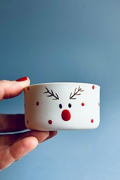 a hand holding a white cup with red and black polka dots on it, decorated like a reindeer's head