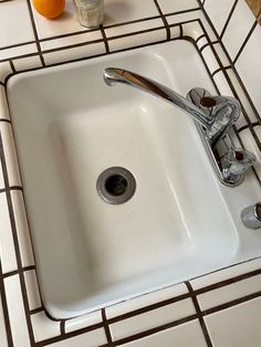 a white sink sitting on top of a tiled counter next to an orange and toothbrush