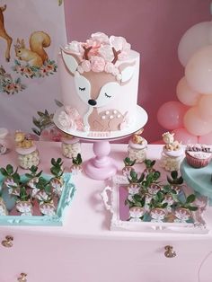 a pink table topped with a cake and cupcakes