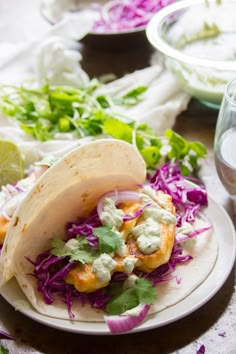 two tacos are sitting on a plate with coleslaw and lime wedges