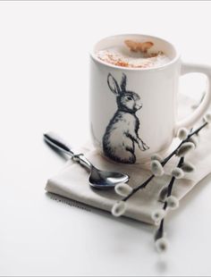 a coffee cup with a bunny drawn on it and some spoons next to it