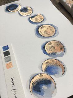 a drawing of phases of the moon in blue and gold on white paper with watercolor pencils