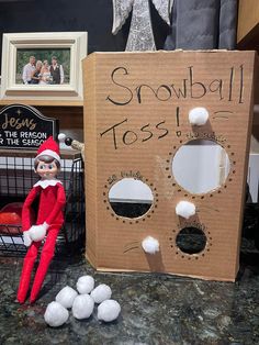 an elf is sitting in front of a cardboard box that says snowball toss