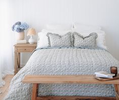 a bed with white and blue comforter in a bedroom next to a table with flowers on it