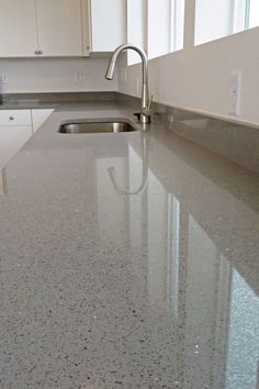 Close up of a countertop that is gray with black and silver flecks in it. Undermount sink with arched faucet and white cabinets with silver pulls are in the background Sparkly Quartz Countertops, Kitchen Sinks With White Countertops, White Countertops With Sparkle, Sparkly White Countertops, Non White Kitchen Countertops, Quartz Kitchen Countertops Sparkle White Cabinets, Modern Kitchen Cabinets White Grey Marble Countertops