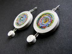 two white earrings with multicolored swirls on them sitting on a black surface