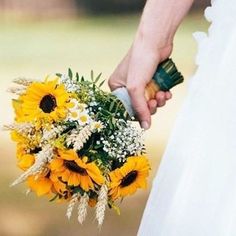 a bride holding a bouquet of sunflowers and baby's breath in her hand