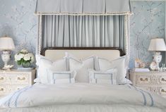 a white bed with blue trim and pillows in a bedroom next to a lamp on a dresser