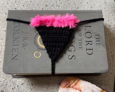 a book with a crocheted black triangle and pink feather on it next to a pair of scissors