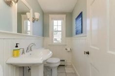 a white bathroom with blue walls and tile flooring, along with a toilet and sink