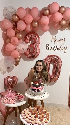 a woman standing in front of a table filled with cakes and cupcakes next to balloons