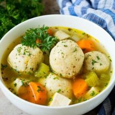 a white bowl filled with soup and dumplings on top of a blue towel next to parsley