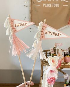 a person holding two pink and white birthday flags in front of a table with flowers