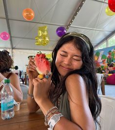 a woman sitting at a table with a piece of watermelon in her hand