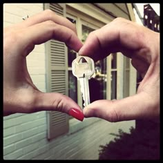 two hands making a heart shape with a house in the background and a key to each other