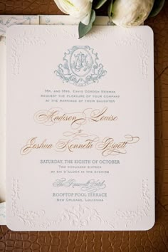 the wedding stationery is laid out on top of a brown leather surface with white flowers