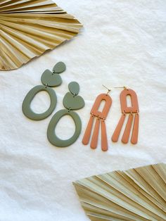 three pairs of earrings sitting on top of a white table next to palm leaf fan