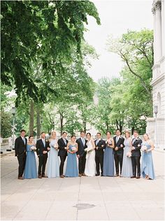 a group of people standing next to each other in front of trees and bushes on a sidewalk