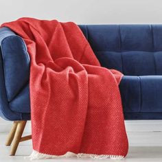 a blue couch with a red blanket sitting on it's back next to a white wall