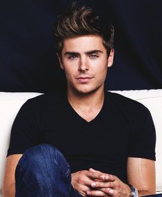 a young man sitting on top of a white couch next to a blue wall and holding his hands together